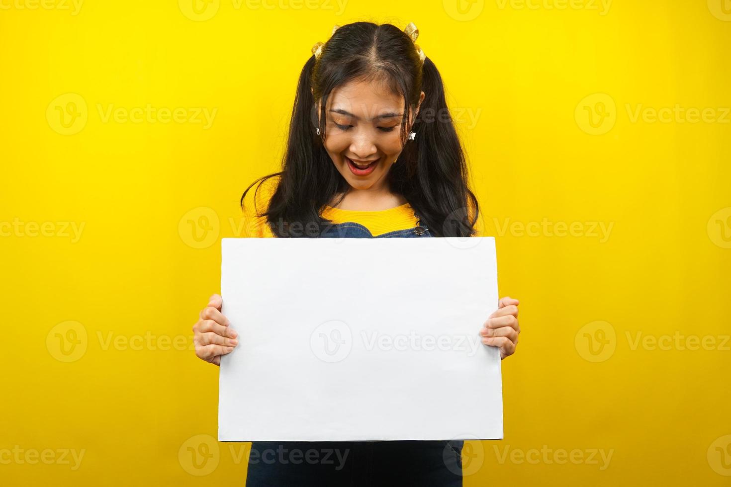 hübsche und süße junge Frau, die fröhliche leere leere Banner, Plakate, weiße Tafeln, leere Schilder, weiße Werbetafeln hält, etwas im Kopierraum präsentiert, Werbung foto