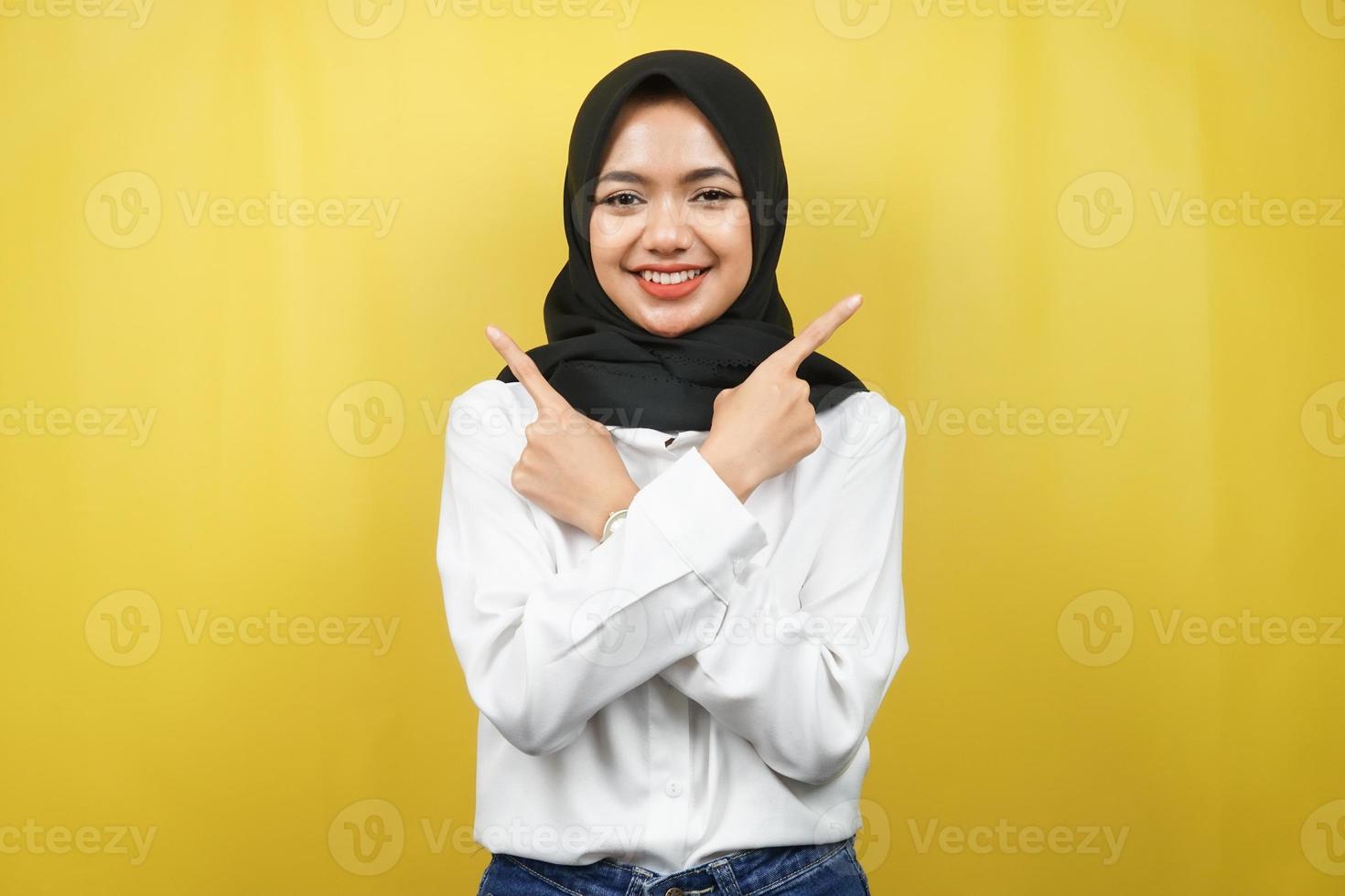 schöne junge asiatische muslimische frau, die selbstbewusst, enthusiastisch, fröhlich lächelt, mit den händen, die auf leeren raum zeigen, etwas präsentieren, die kamera einzeln auf gelbem hintergrund betrachtend, werbekonzept foto