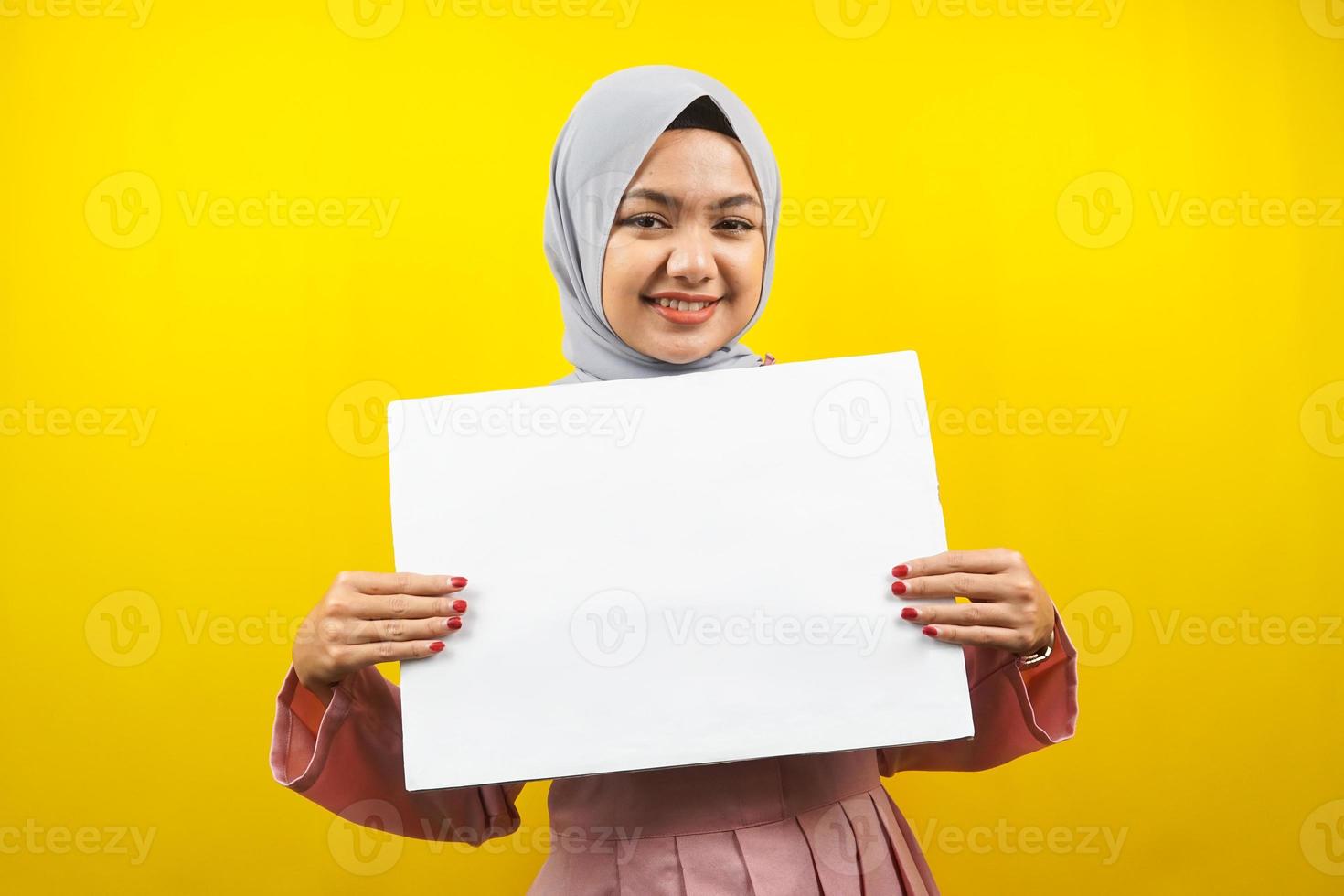 hübsche junge muslimische Frau, die fröhliche leere leere Banner, Plakate, weiße Tafeln, leere Schilder, weiße Werbetafeln hält, etwas im Kopierraum präsentiert, Werbung foto