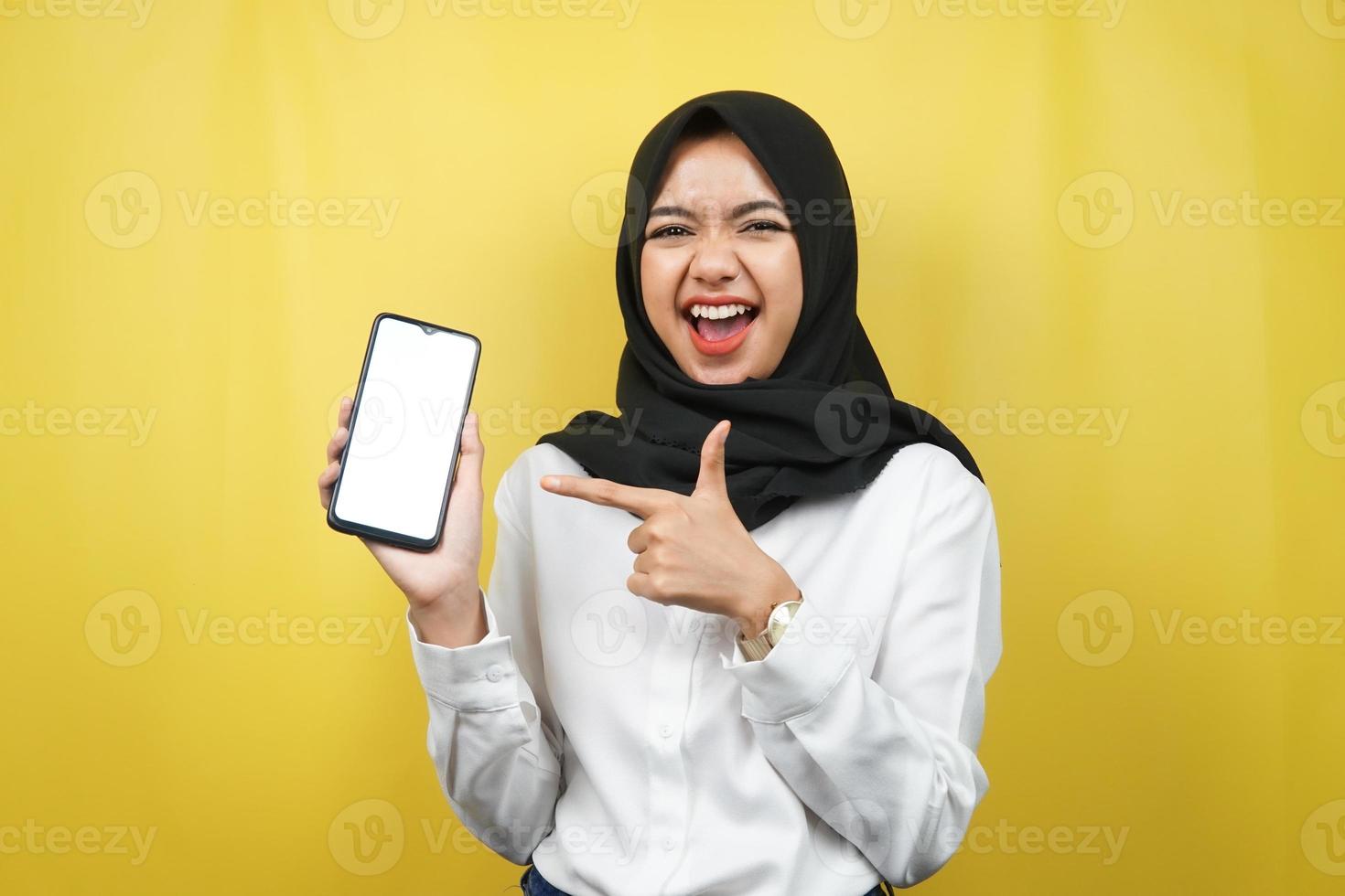 schöne junge asiatische muslimische frau schockiert, überrascht, wow-ausdruck, hand hält smartphone mit weißem oder leerem bildschirm, fördert app, fördert produkt, präsentiert etwas, isoliert foto