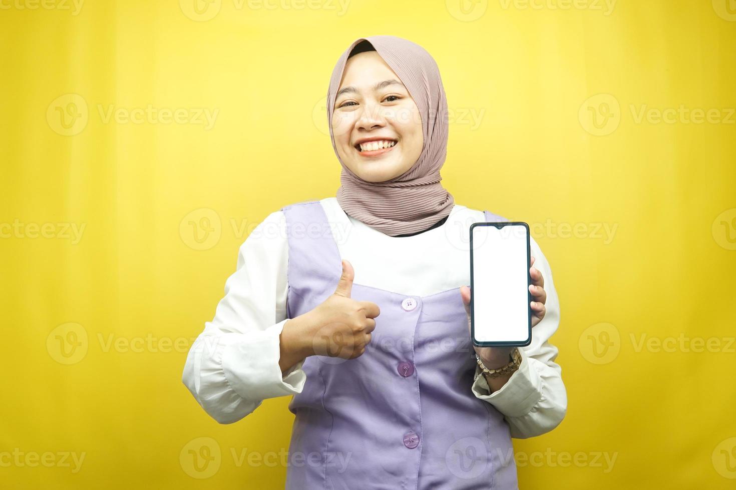 Schöne junge asiatische muslimische Frau, die selbstbewusst und aufgeregt mit den Händen lächelt, die Smartphone halten, Bewerbung fördern, OK-Zeichen-Hand, gute Arbeit, Erfolg, isoliert auf gelbem Hintergrund foto