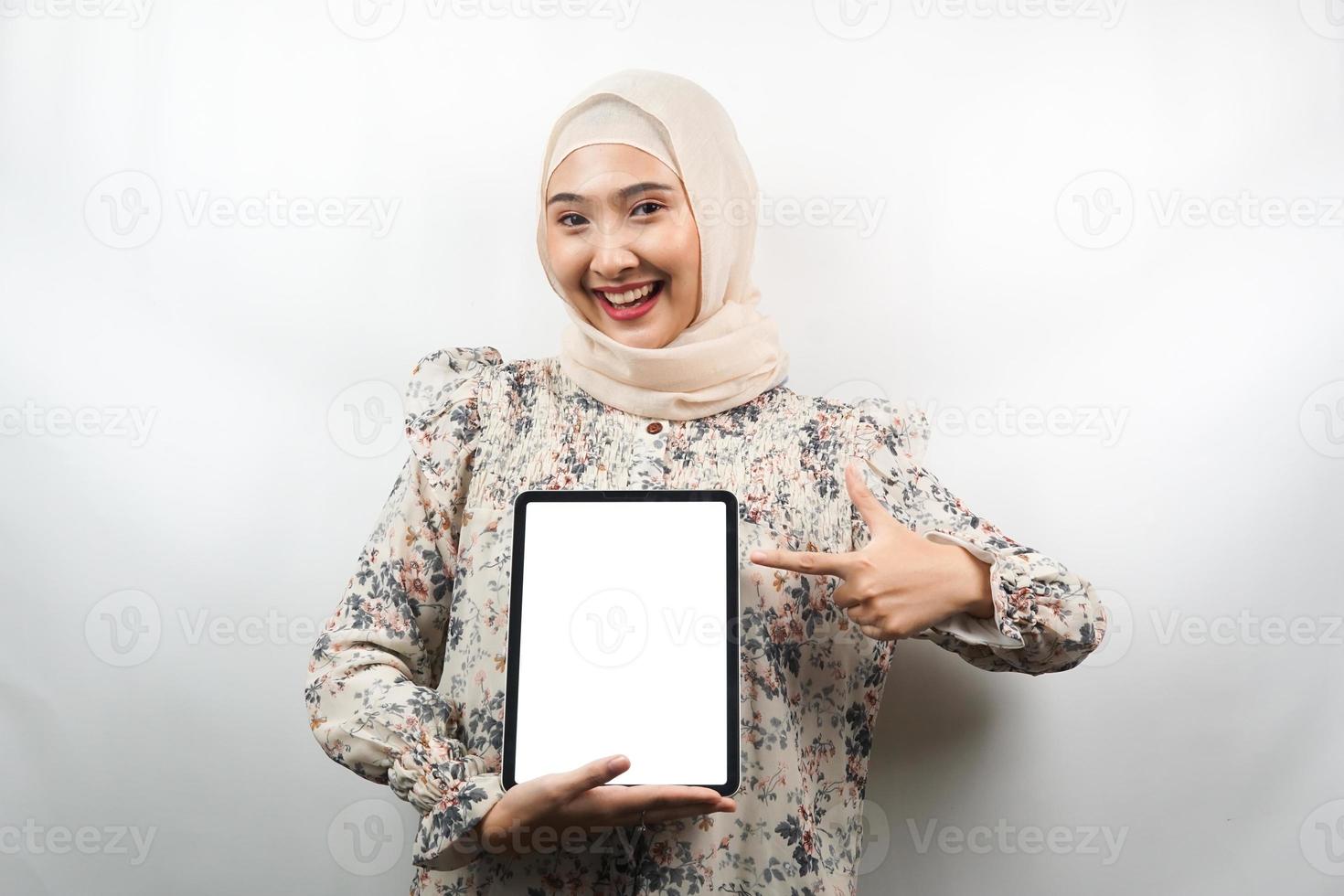 schöne junge asiatische muslimische frau lächelnd, aufgeregt und fröhlich, die tablette mit weißem oder leerem bildschirm hält, app fördert, produkt fördert, etwas präsentiert, isoliert auf weißem hintergrund foto