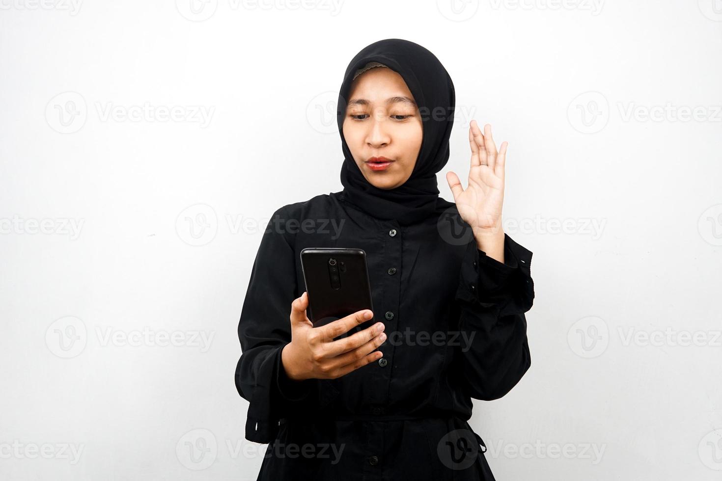 schöne junge asiatische muslimische frau schockiert, überrascht, mit den händen, die das smartphone halten, das smartphone betrachten, die promo betrachten, einzeln auf weißem hintergrund, werbekonzept foto