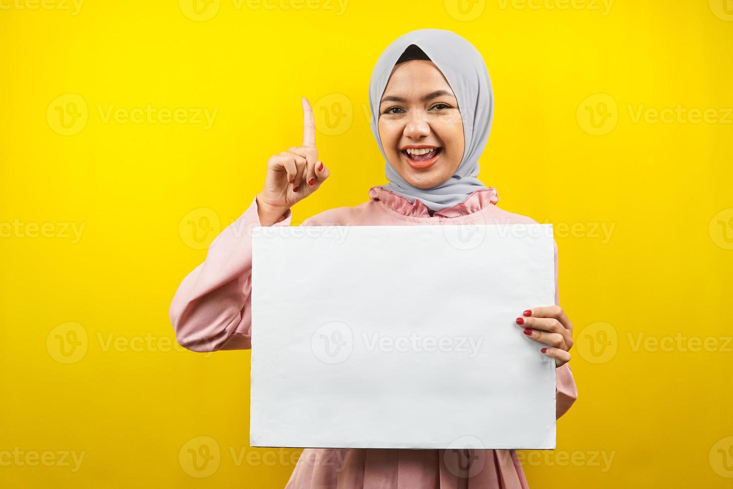 hübsche junge muslimische Frau, die fröhliche leere leere Banner, Plakate, weiße Tafeln, leere Schilder, weiße Werbetafeln hält, etwas im Kopierraum präsentiert, Werbung foto