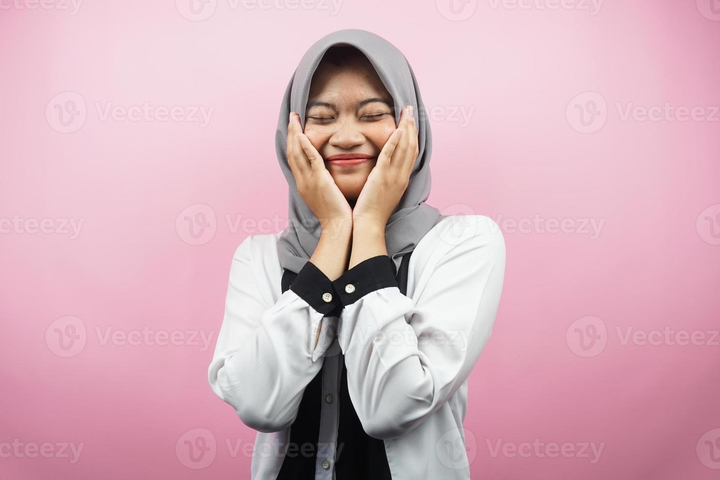schöne junge asiatische muslimische Frau, die glücklich lächelt, süß, sich wohl fühlt, sich umsorgt fühlt, sich gut fühlt, mit Händen, die Wangen einzeln auf rosafarbenem Hintergrund halten foto