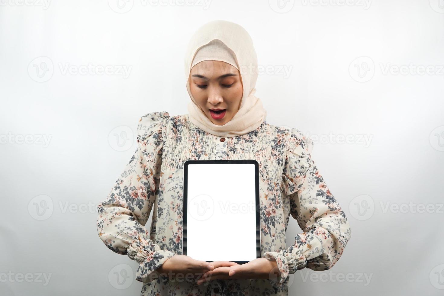 schöne junge asiatische muslimische frau lächelnd, aufgeregt und fröhlich, die tablette mit weißem oder leerem bildschirm hält, app fördert, produkt fördert, etwas präsentiert, isoliert auf weißem hintergrund foto