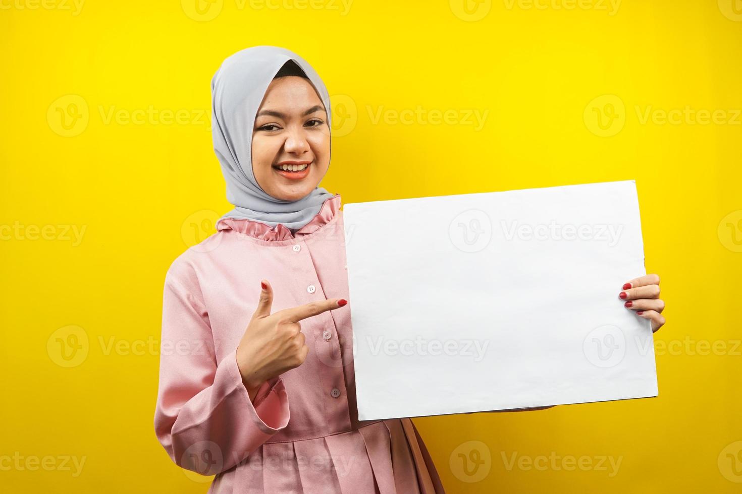 hübsche junge muslimische Frau, die fröhliche leere leere Banner, Plakate, weiße Tafeln, leere Schilder, weiße Werbetafeln hält, etwas im Kopierraum präsentiert, Werbung foto