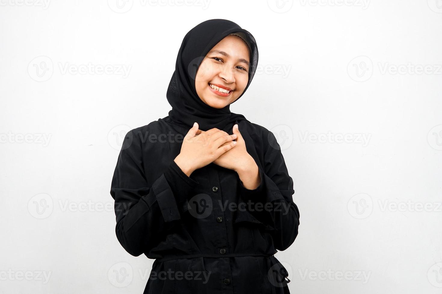 schöne junge asiatische muslimische frau, die überrascht und fröhlich lächelt, mit den händen, die die brust halten, aufgeregt, nicht erwartet, die kamera einzeln auf weißem hintergrund betrachtend foto