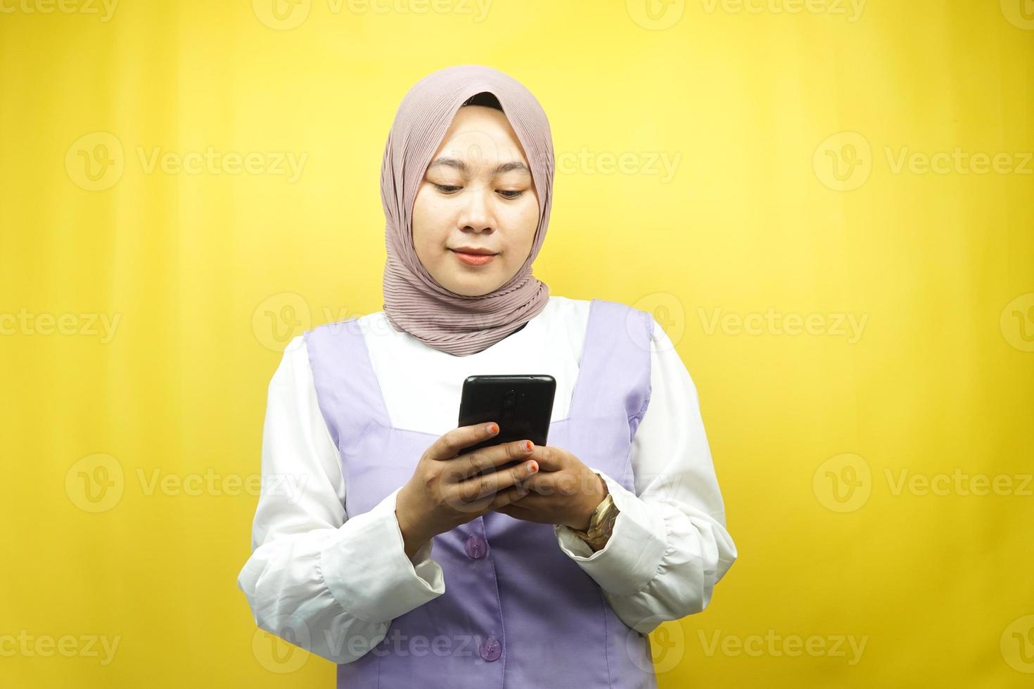 schöne asiatische junge muslimische frau, die smartphone isoliert auf gelbem hintergrund hält foto