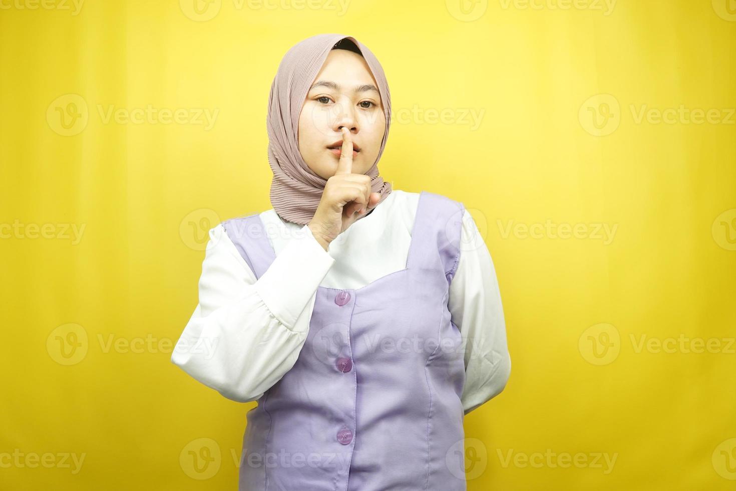 schöne asiatische junge muslimische frau mit finger auf dem mund, sagt, sie soll leise sein, keinen lärm machen, stimme senken, nicht sprechen, isoliert auf gelbem hintergrund foto