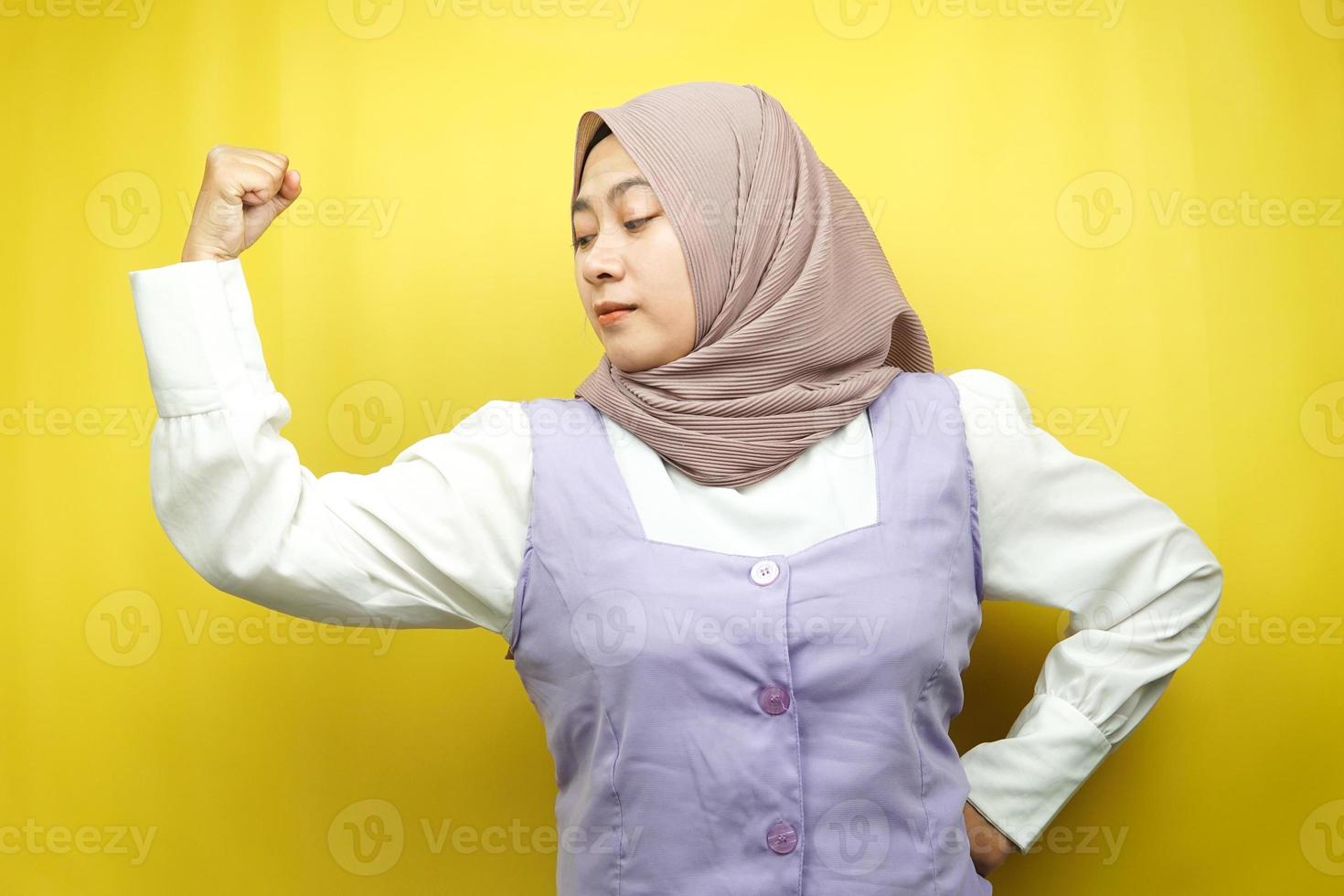 schöne asiatische junge muslimische frau mit angehobenen muskeln, kraftzeichenarme, isoliert auf gelbem hintergrund foto