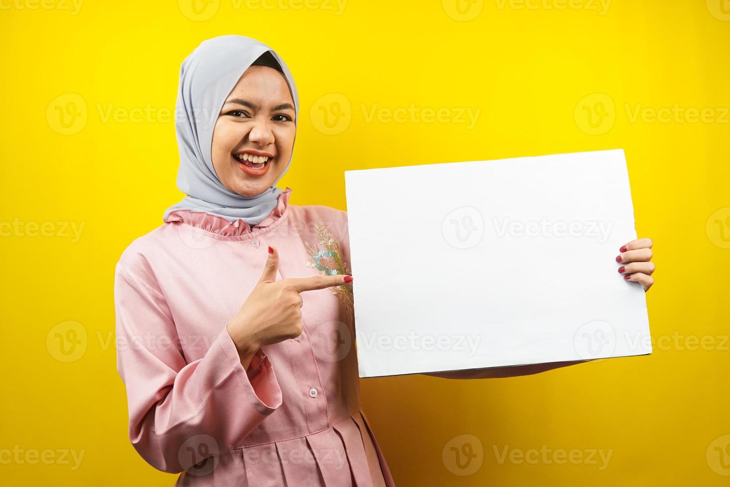 hübsche junge muslimische Frau, die fröhliche leere leere Banner, Plakate, weiße Tafeln, leere Schilder, weiße Werbetafeln hält, etwas im Kopierraum präsentiert, Werbung foto