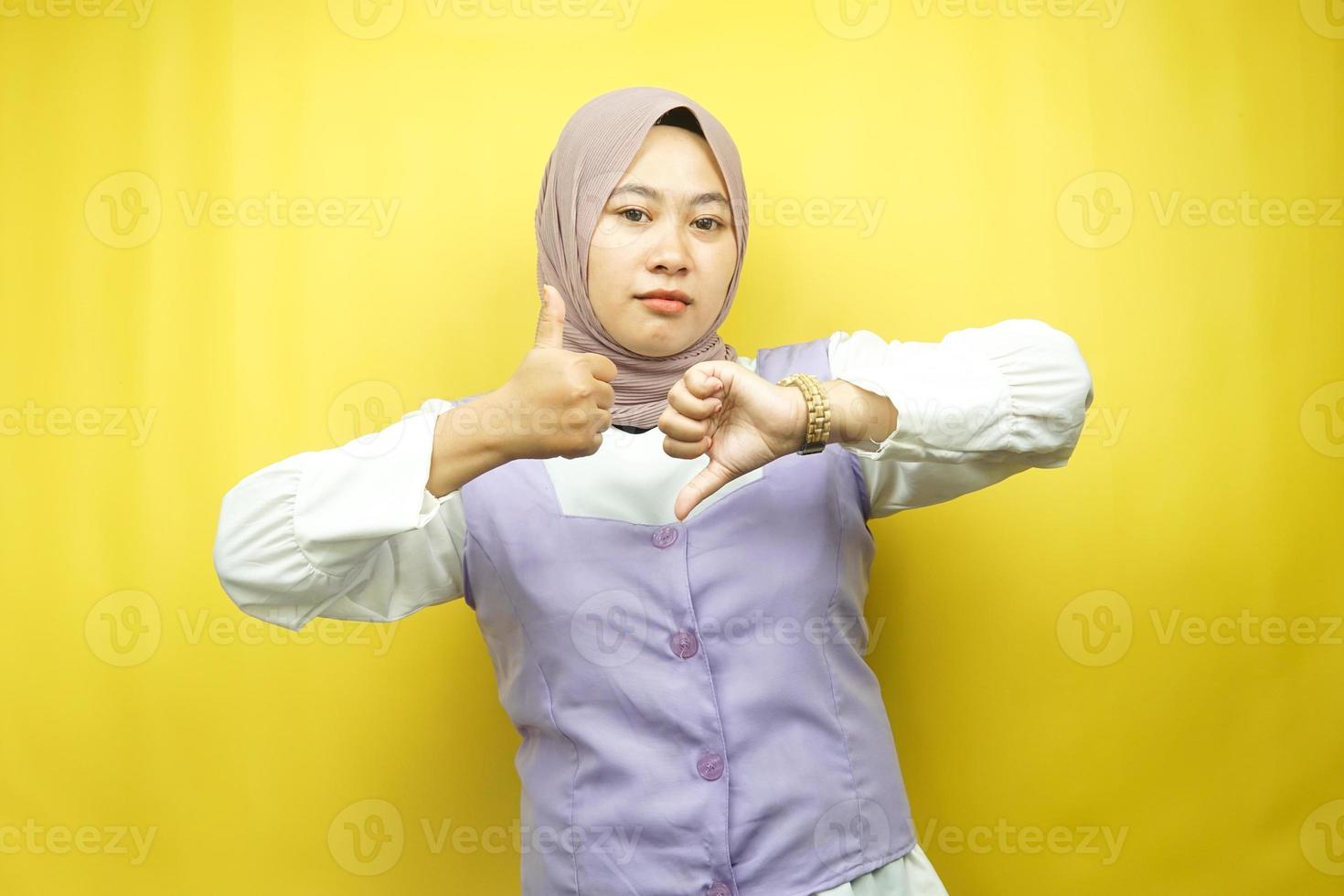 schöne asiatische junge muslimische frau mit handzeichen wie oder abneigung, ja oder nein, glücklich oder traurig, vergleicht zwei dinge, einzeln auf gelbem hintergrund foto