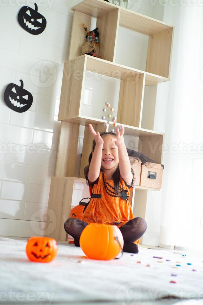 Portrait asiatisches kleines Mädchen wirft und isst Süßigkeiten und Schokolade aus Süßes oder Saures mit Halloween-Thema im Hintergrund foto