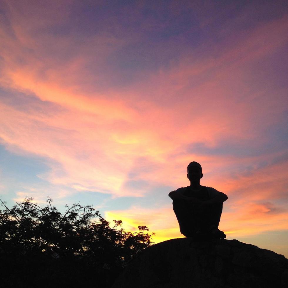 Silhouette eines Mannes, der vor einem orangefarbenen Himmelshintergrund sitzt. foto