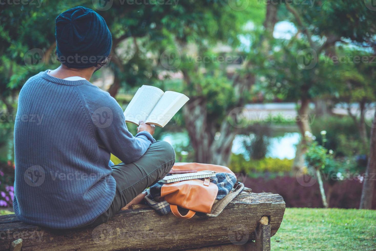 der junge Mann las im Park ein Buch. zwischen den natürlichen Bäumen und dem schönen Blumengarten foto