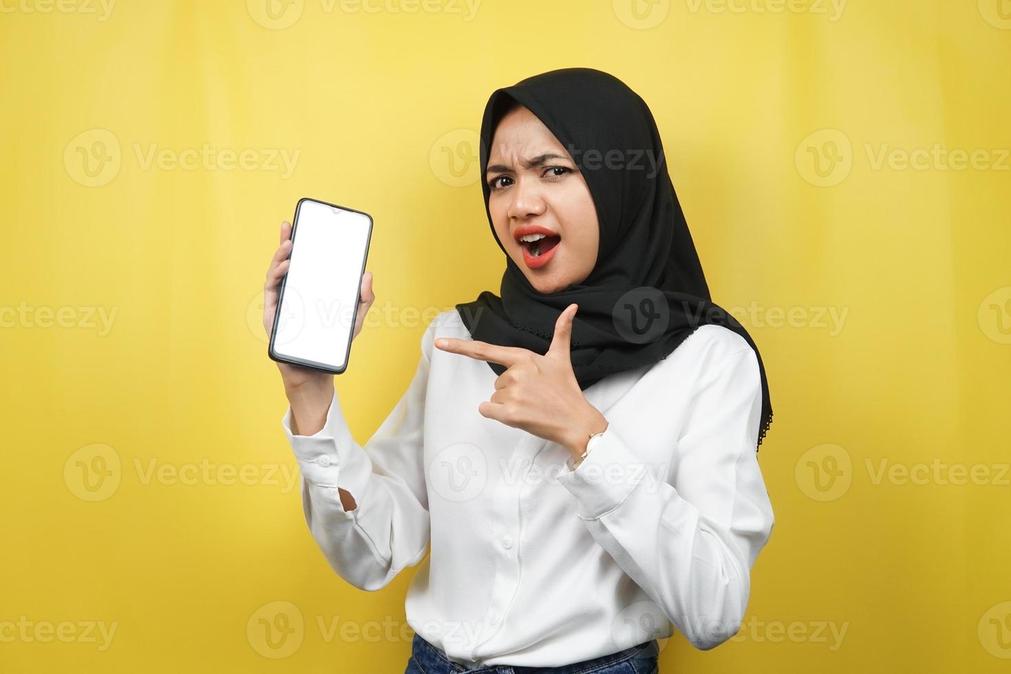 schöne junge asiatische muslimische frau schockiert, überrascht, wow-ausdruck, hand hält smartphone mit weißem oder leerem bildschirm, fördert app, fördert produkt, präsentiert etwas, isoliert foto