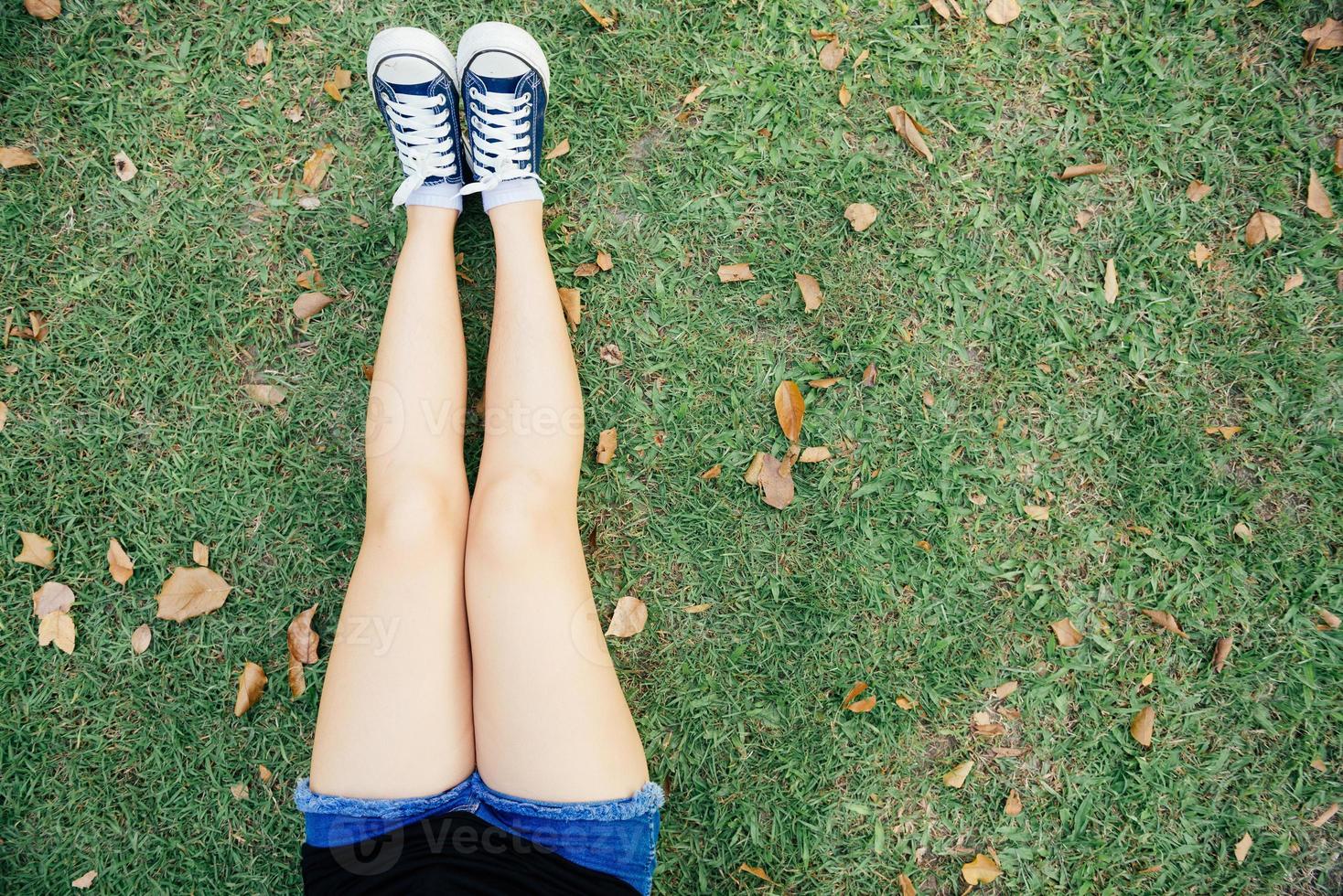 Nahaufnahme einer jungen asiatischen Frau, die einsam auf dem grünen Gras im öffentlichen Park sitzt. Junge Frau, die im Park nah oben auf ihren Beinen sitzt, lag direkt auf dem Gras. Outdoor-Aktivität im Parkkonzept foto