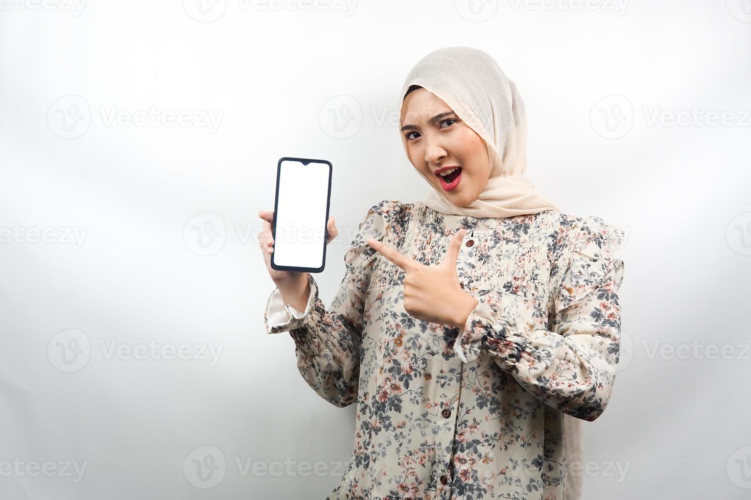 schöne junge asiatische muslimische frau schockiert, überrascht, wow-ausdruck, hand hält smartphone mit weißem oder leerem bildschirm, fördert app, fördert produkt, präsentiert etwas, isoliert foto