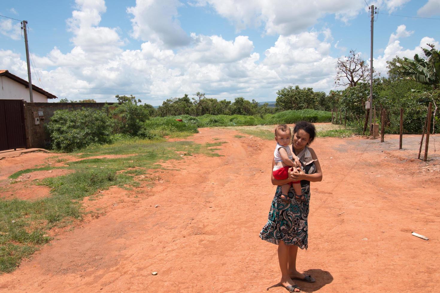 planaltina, goias, brasilien, 12. november 2021 eine arme mutter hält ihr kind mitten auf einer unbefestigten straße in der nähe ihres hauses foto