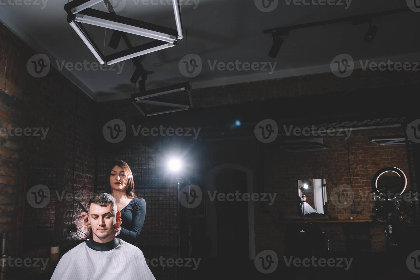 Schöne Friseurin, die in einem Friseurladen die Haare des Kunden mit einer Schere schneidet foto