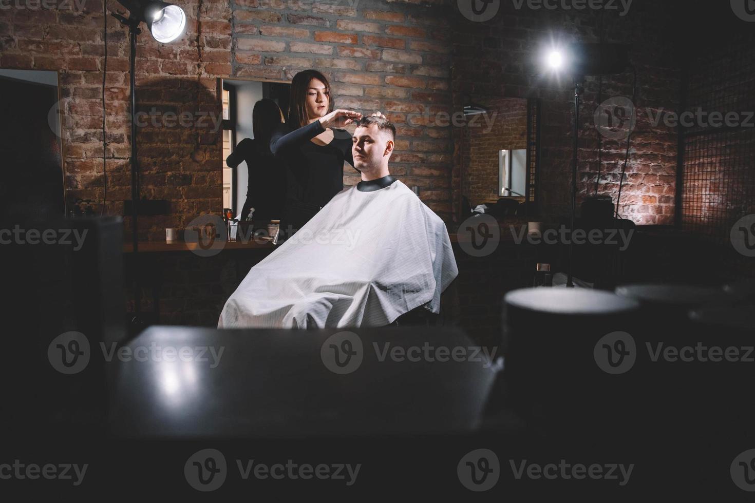 Schöne Friseurin, die in einem Friseurladen die Haare des Kunden mit einer Schere schneidet foto