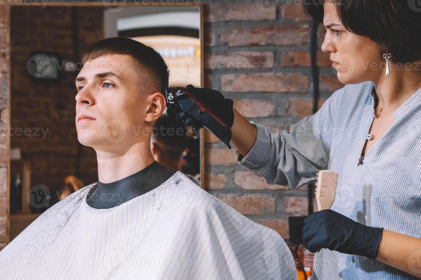 Schöne Friseurin rasiert den Kopf des Kunden mit einem elektrischen Trimmer im Friseurladen. Werbe- und Friseurkonzept foto