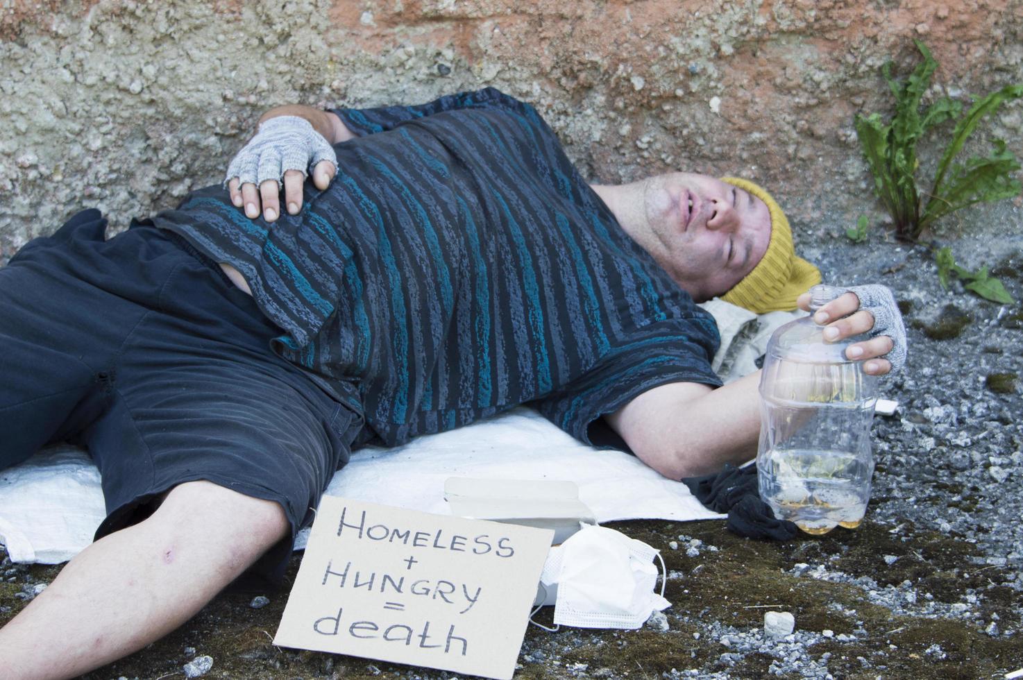 Ein betrunkener Obdachloser schläft auf der Straße und hält eine Bierflasche in der Hand. Armut, Arbeitslosigkeit, Alkoholismus. foto
