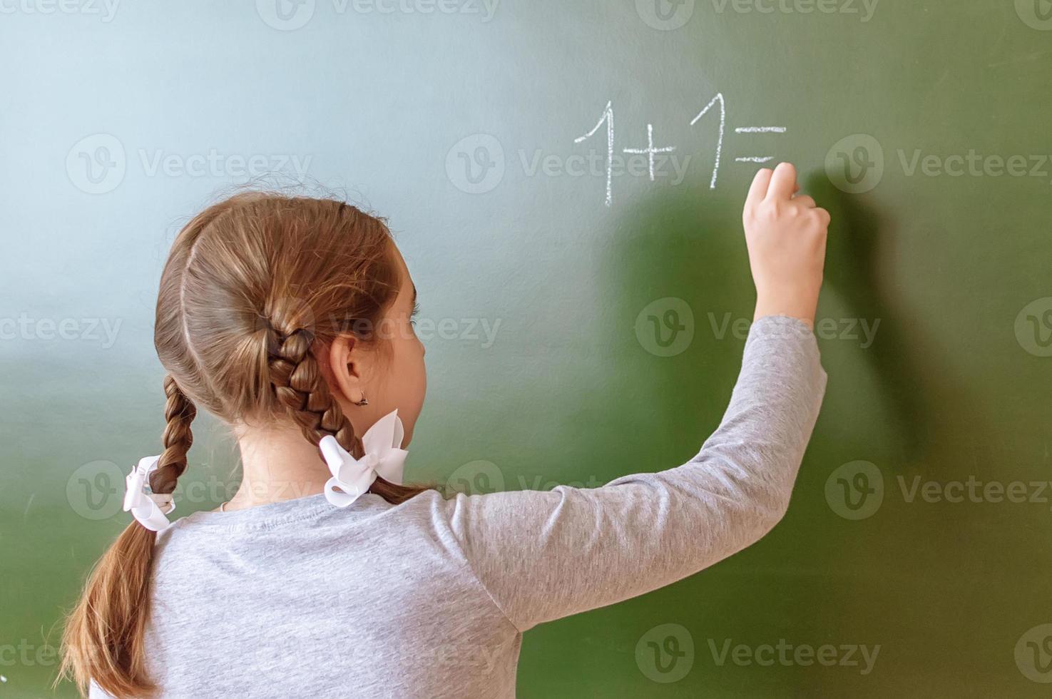 Schulmädchen löst während des Unterrichts eine Matheaufgabe an der Tafel. foto