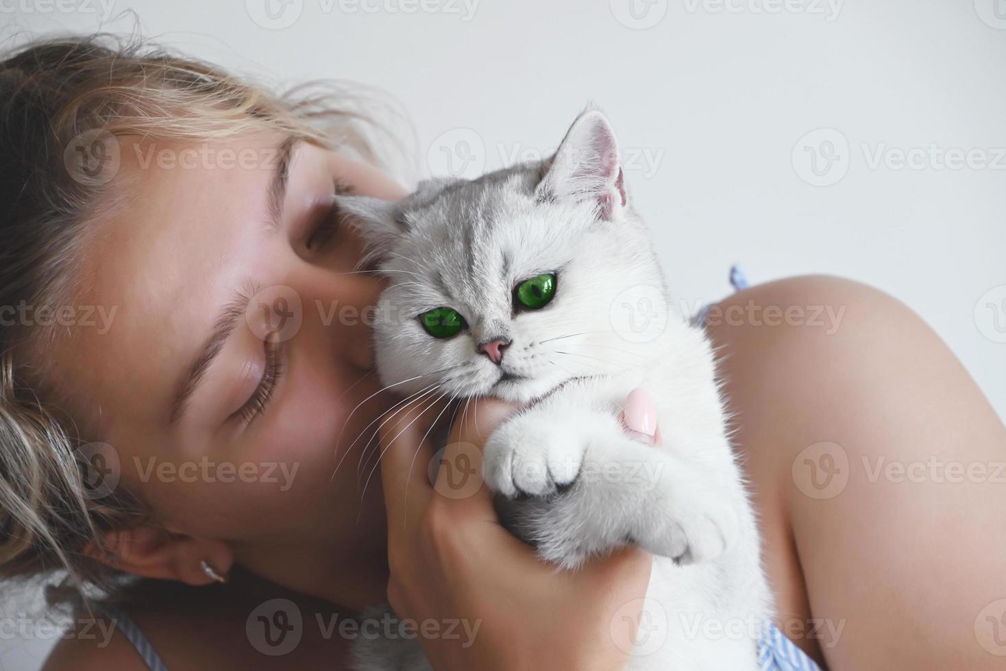 Ein schönes junges Mädchen küsst eine weiße Katze mit grünen Augen. Britisches Silber-Chinchilla. foto