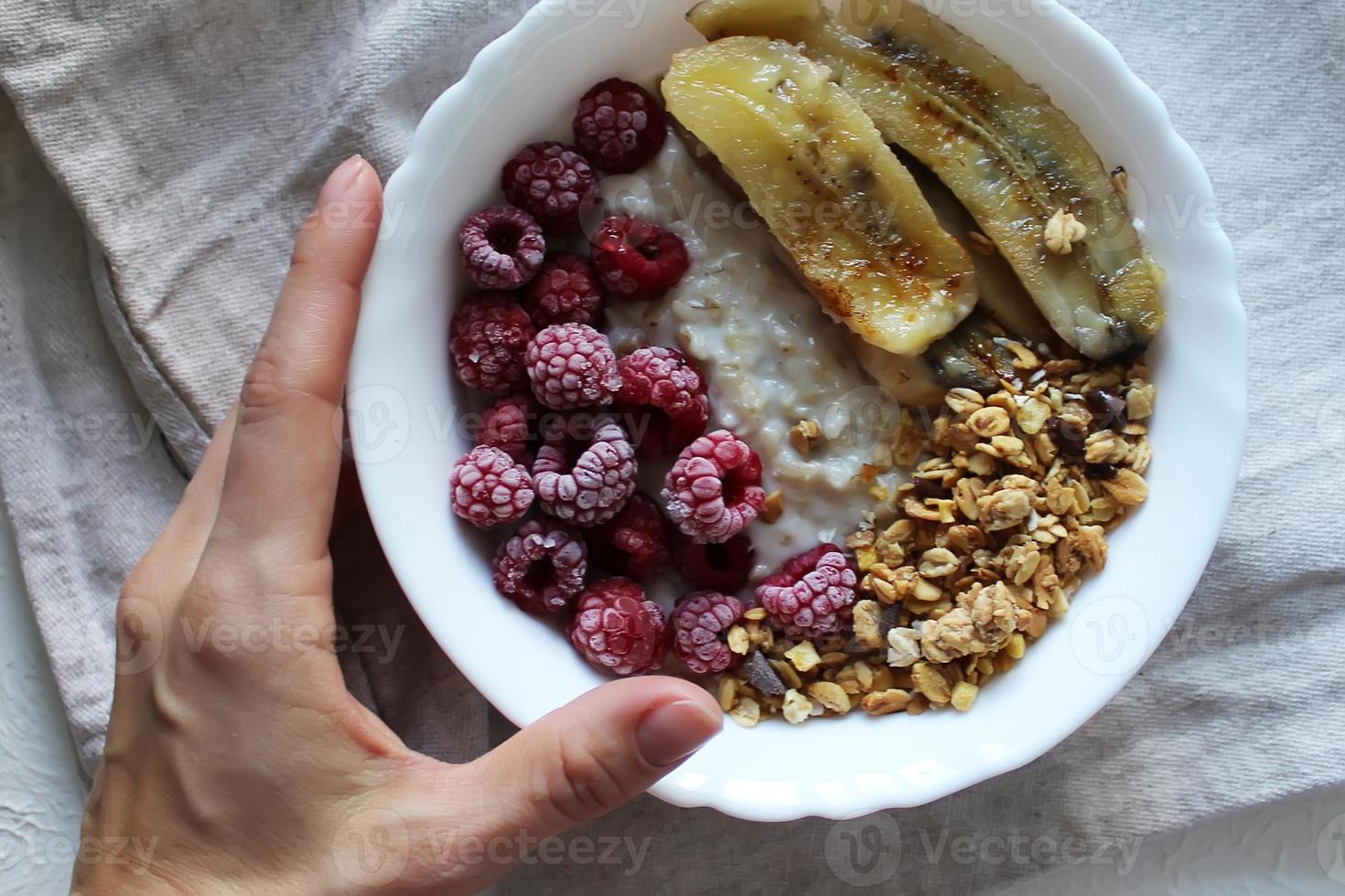 Die Hand des Mädchens hält einen Teller Haferflockenbrei mit Himbeeren und gebratenen Bananen. gesundes Frühstück. foto