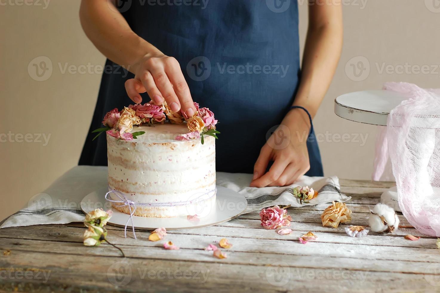 Frauenhände schmücken die Sahnetorte mit frischen Blumen. horizontales Foto. foto