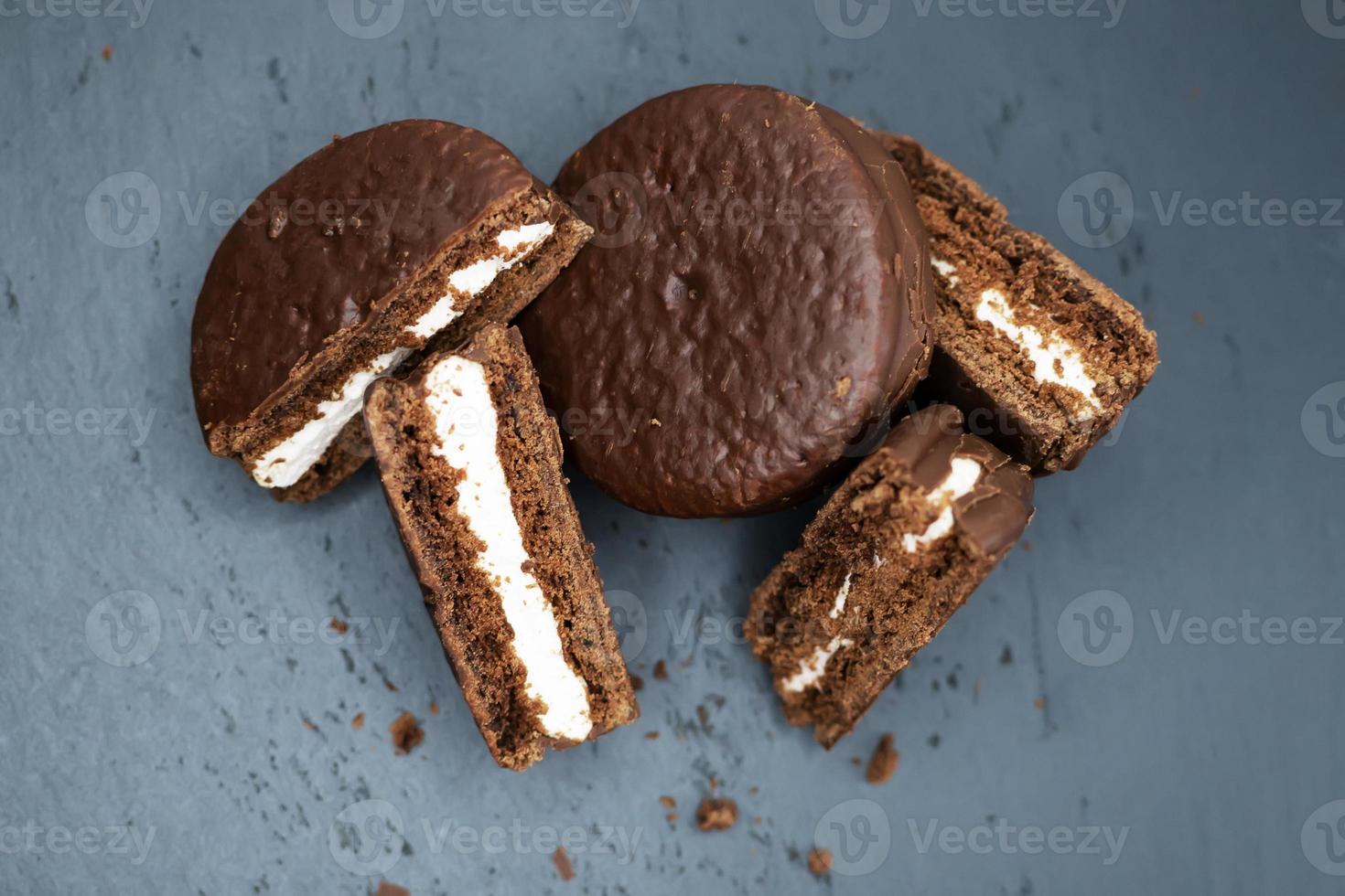 Kekse in Schokoladenglasur und weißer Cremefüllung auf dunklem Hintergrund verstreut. Ansicht von oben. foto