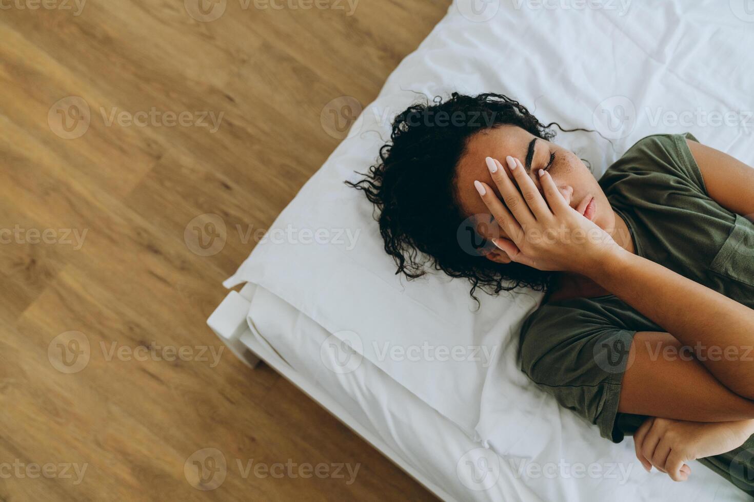 Draufsicht einer afrikanischen unzufriedenen Frau, die ihr Gesicht mit der Hand auf dem Bett bedeckt foto