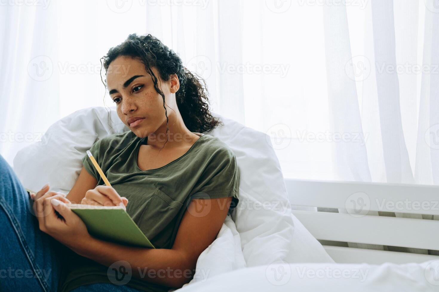 meditative afrikanische frau, die etwas in den notizblock auf dem bett schreibt foto