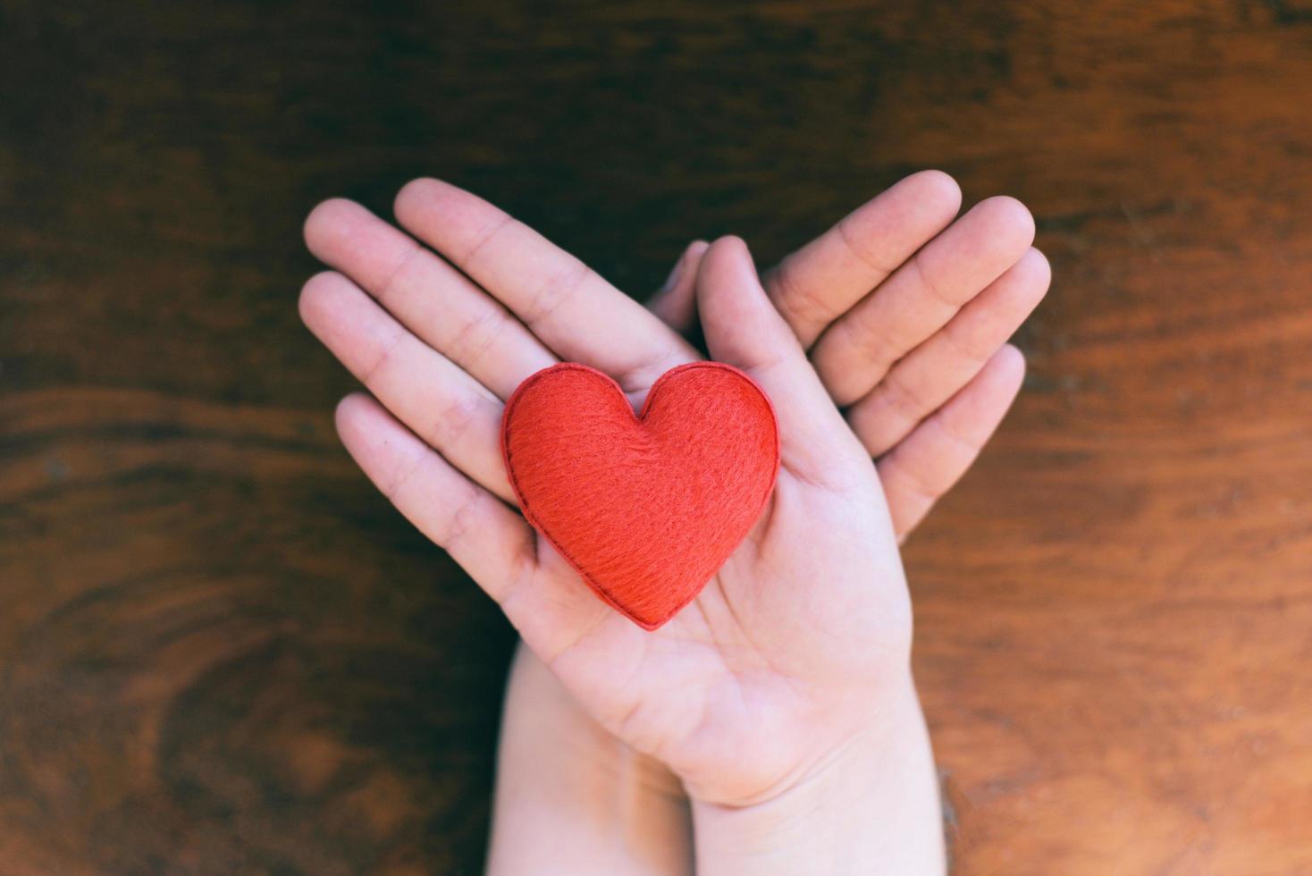 Herz in der Hand für Philanthropie-Konzept - Frau, die zum Valentinstag rotes Herz an den Händen hält oder spendet, um Liebeswärme zu geben, auf Holzhintergrund achten foto