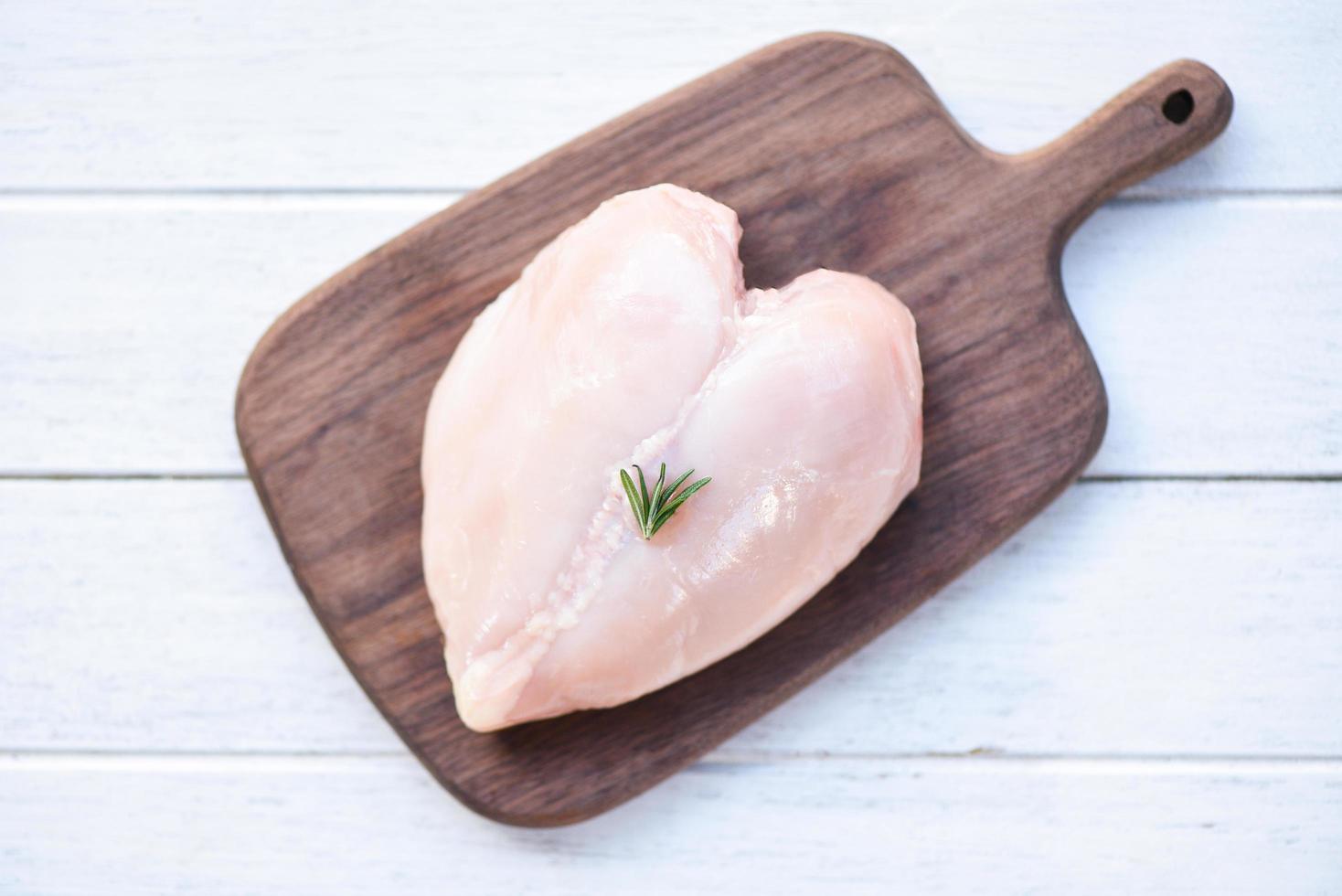 rohes Hühnerfleisch mit Rosmarin auf Holzschneidebrett frisches rohes Hühnerbrustfilet in Herzform auf Holz-Health-Food-Konzept foto