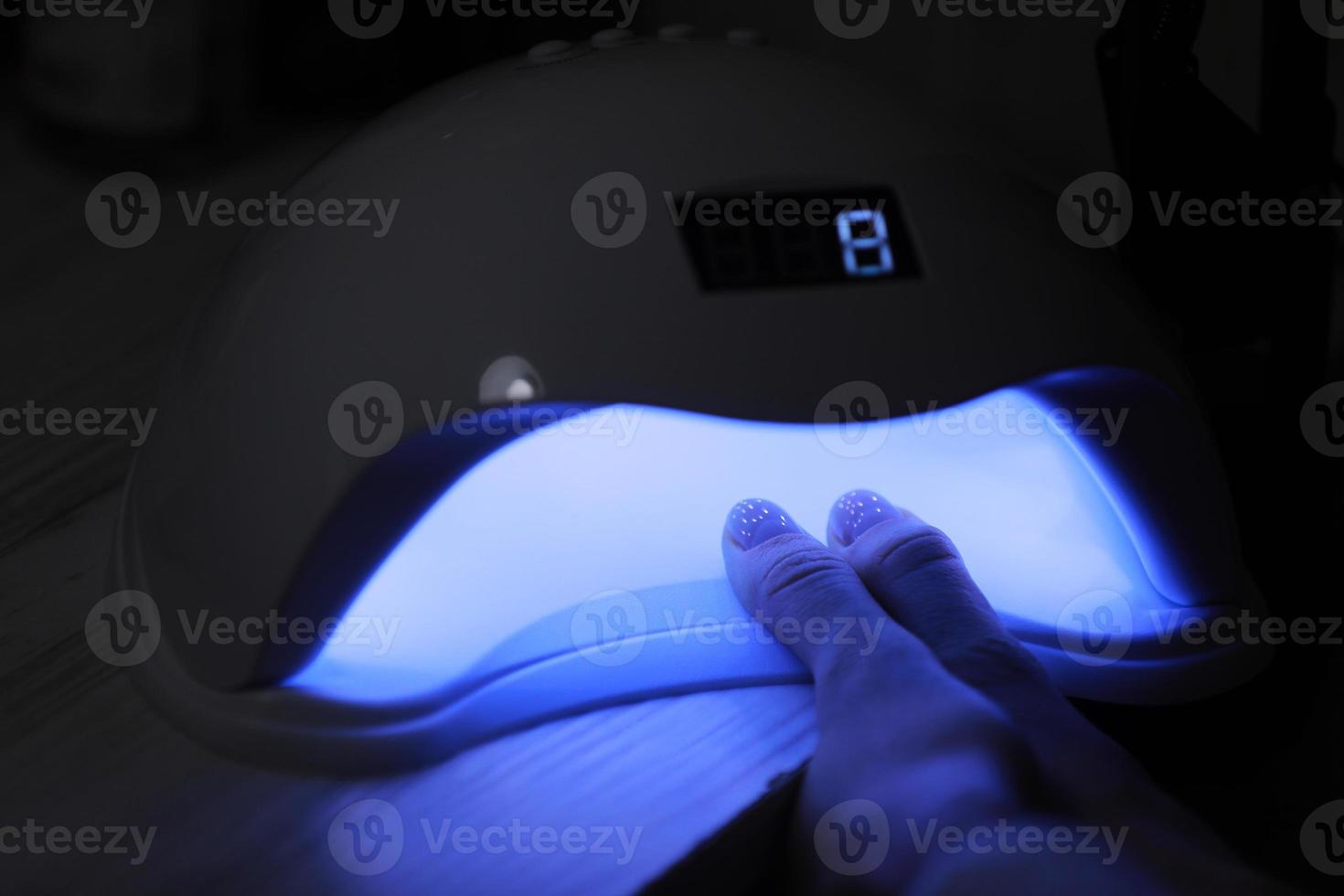 Detailansicht der weiblichen Hände mit Gelpoliturmaniküre. Frau legt Hand in LED-UV-Lampe, um die obere Abdeckung des Nagellacks auszuhärten. UV-Lampe, LED-Nagel foto