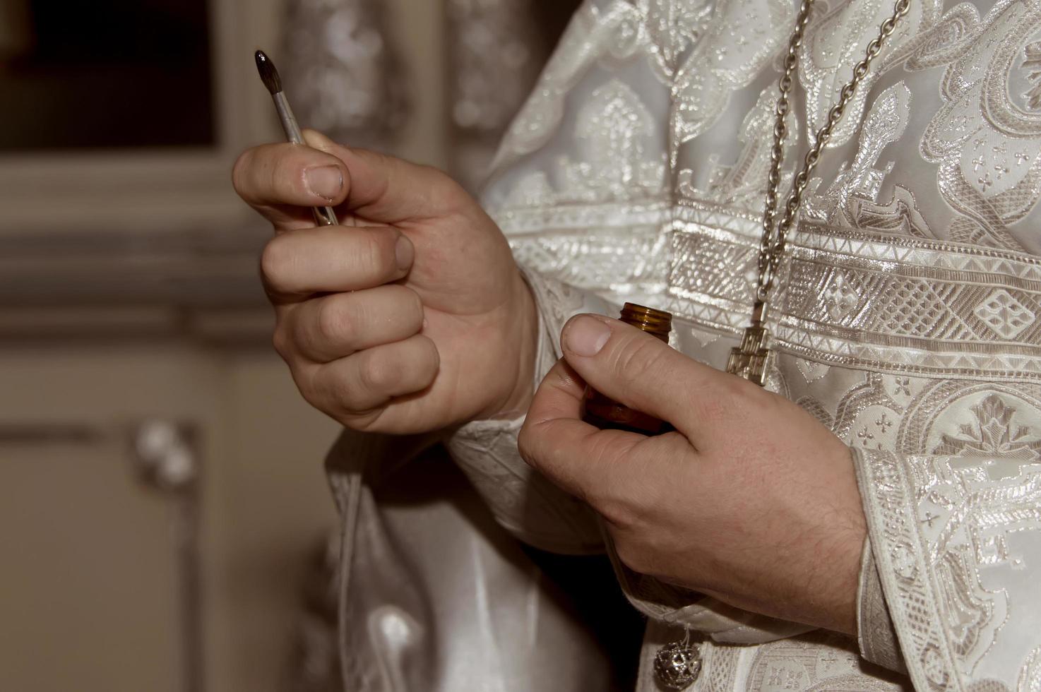 die Hände des Priesters halten einen Pinsel mit salbungsvollem Öl. die Taufzeremonie. Nahansicht. foto