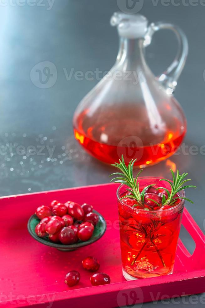 Glas frischer Cranberry-Fruchtsaft mit Rosmarin und sasischer Obstschale in einem roten Tablett, Krug, auf einem grauen Schieferhintergrund foto