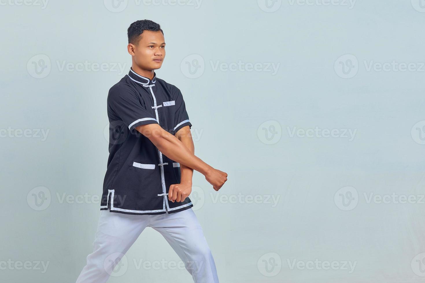 Porträt eines jungen asiatischen Mannes, der einen Taekwondo-Kimono trägt und eine Boxergeste auf grauem Hintergrund zeigt foto