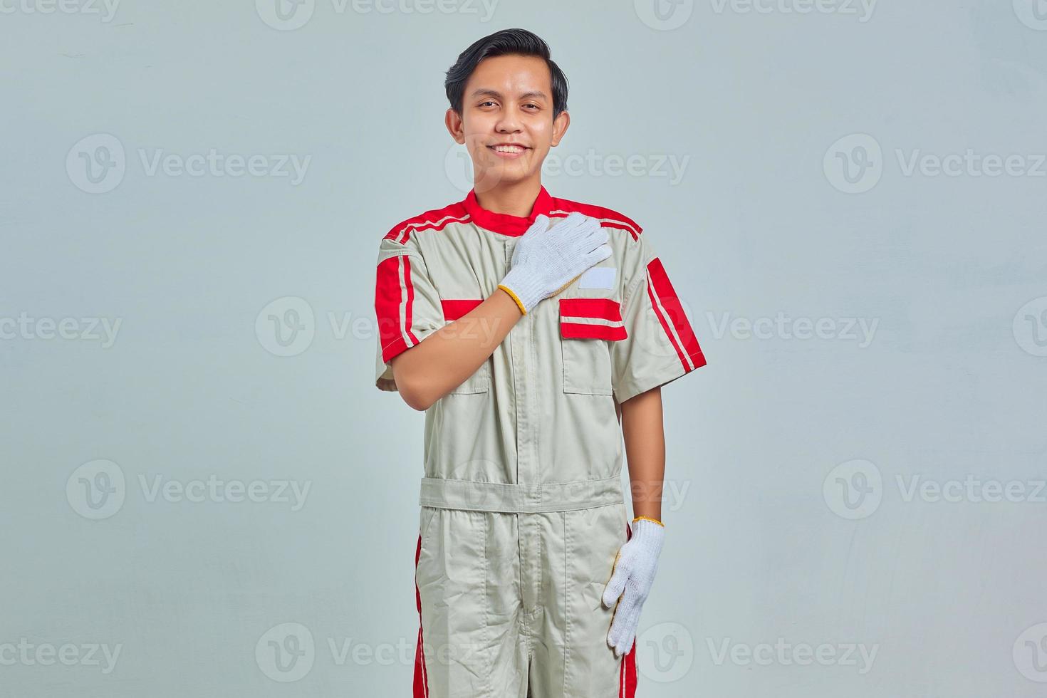 Porträt eines jungen Mechanikers, der mit einem großen Lächeln auf seinem Gesicht grüßt, isoliert auf grauem Hintergrund foto