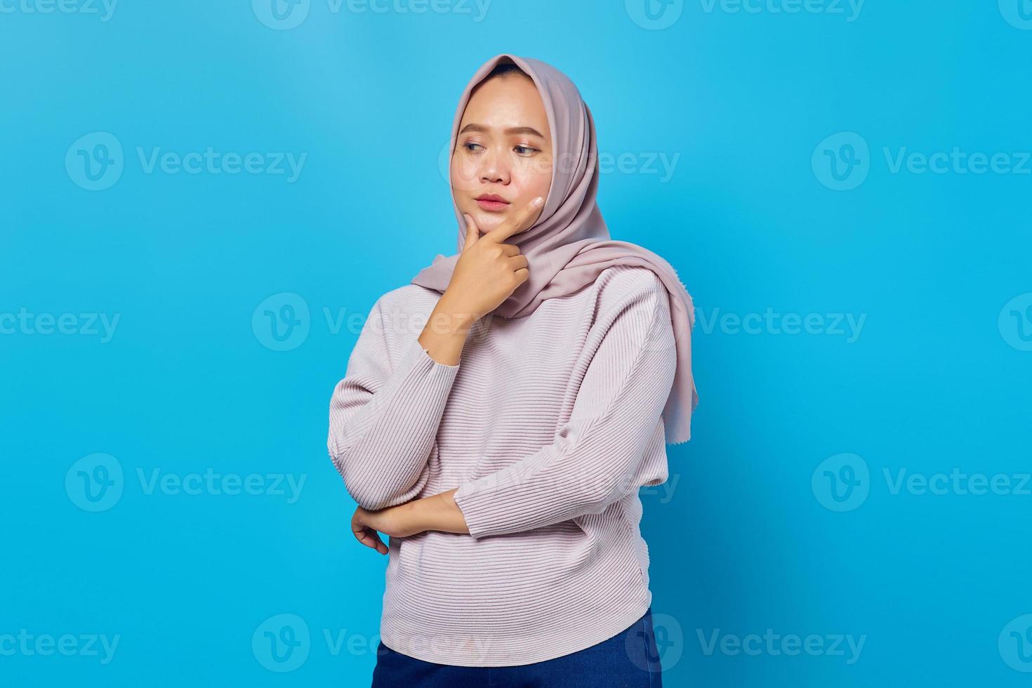 Porträt einer attraktiven asiatischen Frau, die das Kinn über blauem Hintergrund denkt und berührt foto