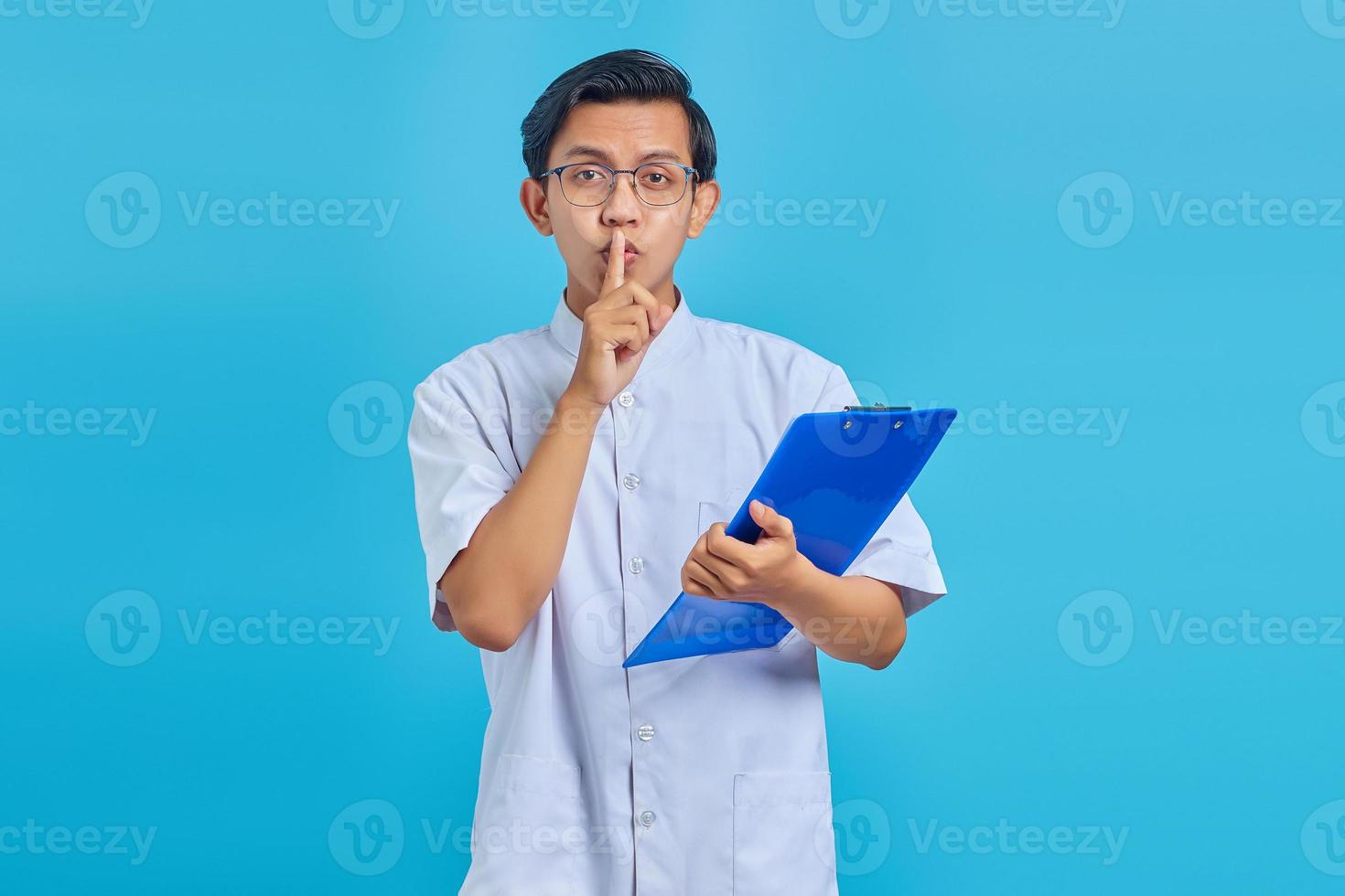 junger Pfleger finger auf den Lippen und macht eine stille Geste auf blauem Hintergrund foto