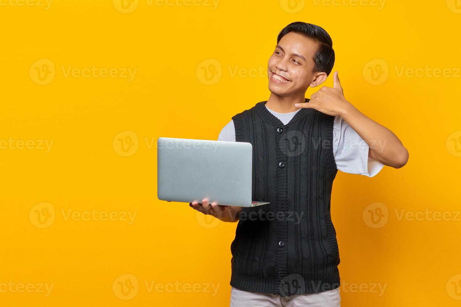 Porträt einer lächelnden jungen Asiatin, die Laptop hält und Telefongeste mit dem Finger macht foto