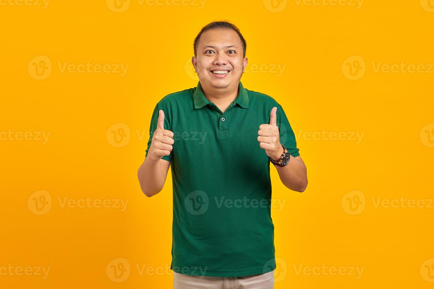 Fröhlicher, gutaussehender asiatischer junger Mann, der die Geste mit dem Daumen nach oben isoliert auf gelbem Hintergrund zeigt foto