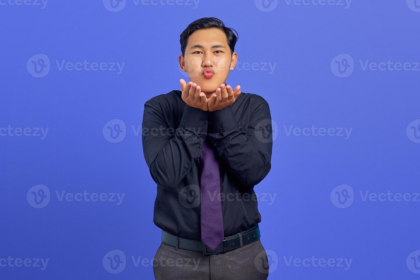 Porträt eines charmanten jungen asiatischen Mannes, der Handflächen hält, senden Luftkuss auf lila Hintergrund foto