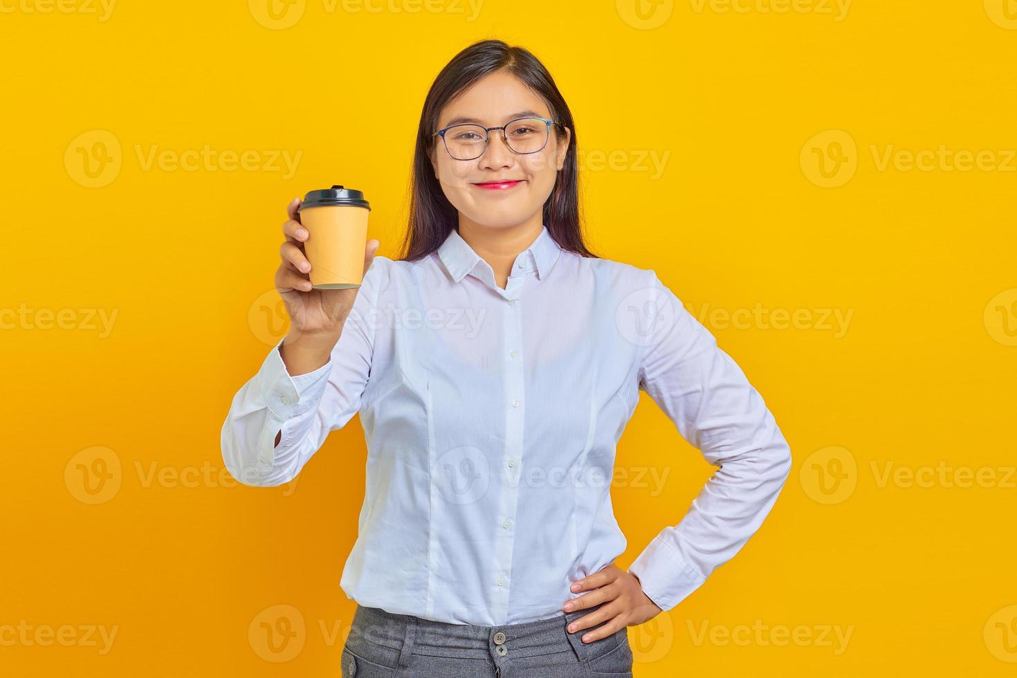 Foto einer lächelnden und fröhlichen asiatischen Geschäftsfrau mit weißem Hemd, die frisch gekaufte Tasse Kaffee auf gelbem Hintergrund hält