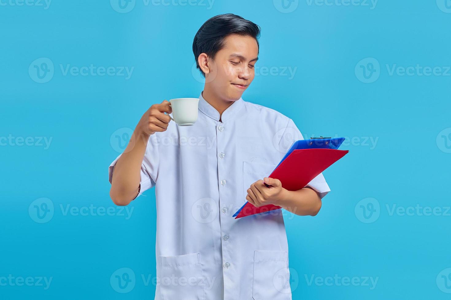lächelnder junger Krankenpfleger, der Ordner und Tasse über blauem Hintergrund hält foto