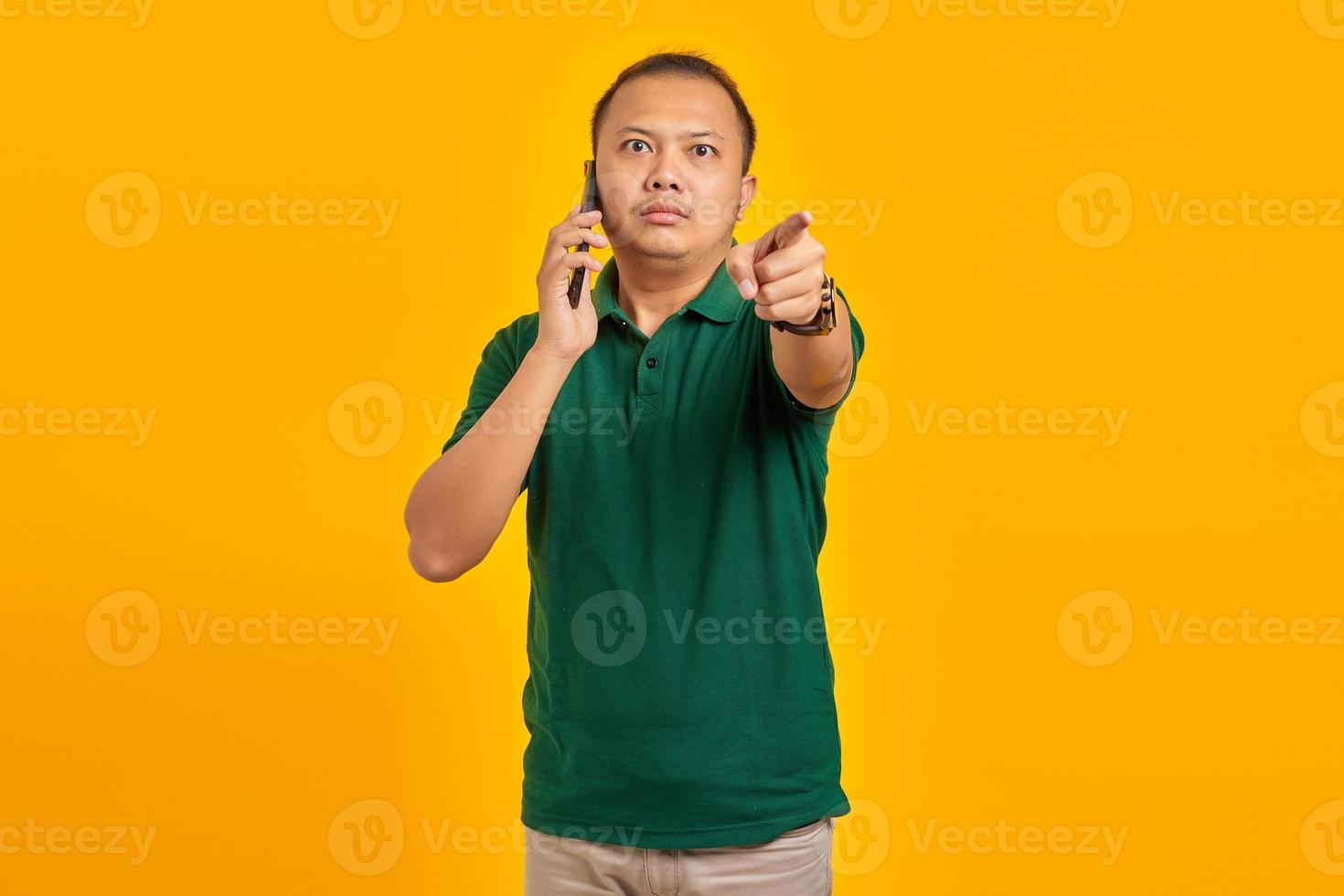 Wütender asiatischer junger Mann, der auf dem Smartphone spricht und Warnzeichen auf gelbem Hintergrund isoliert foto